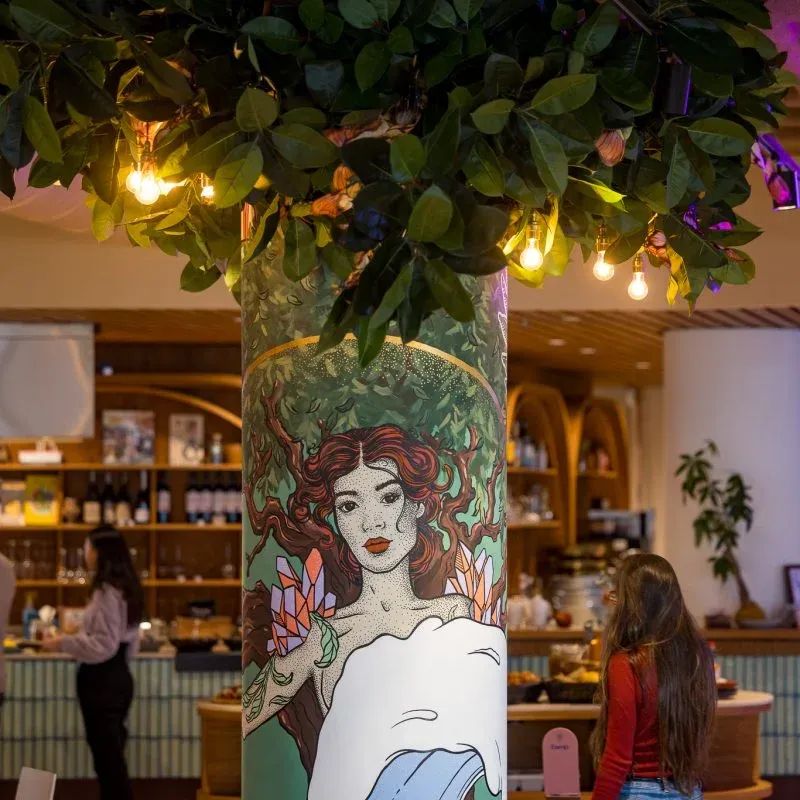 A decorative pillar with a painted woman, green leaves, and illuminated fairy lights.