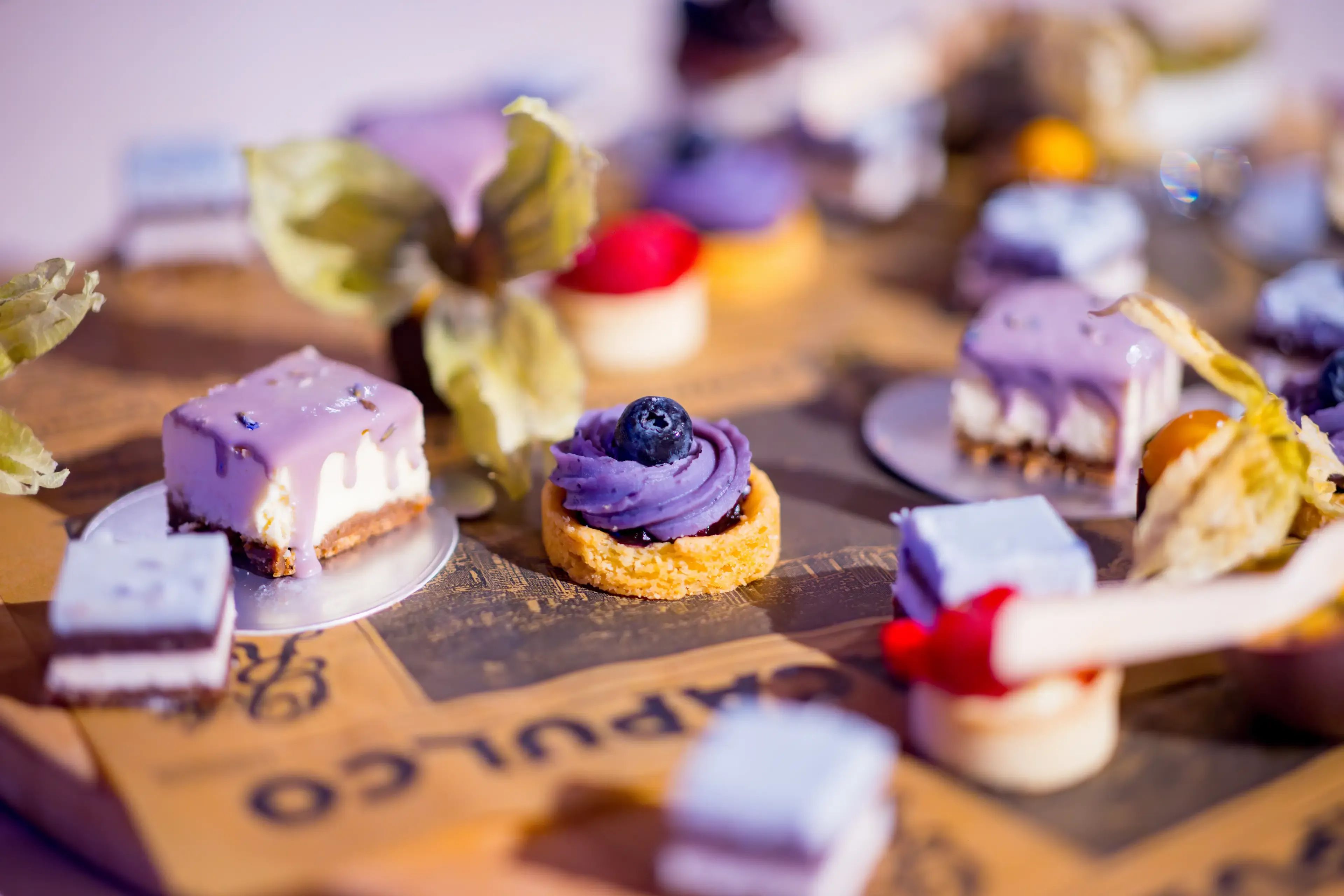 Diverse kleine paarse en witte desserts met bosbessen en kaapse kruisbessen op een houten ondergrond.