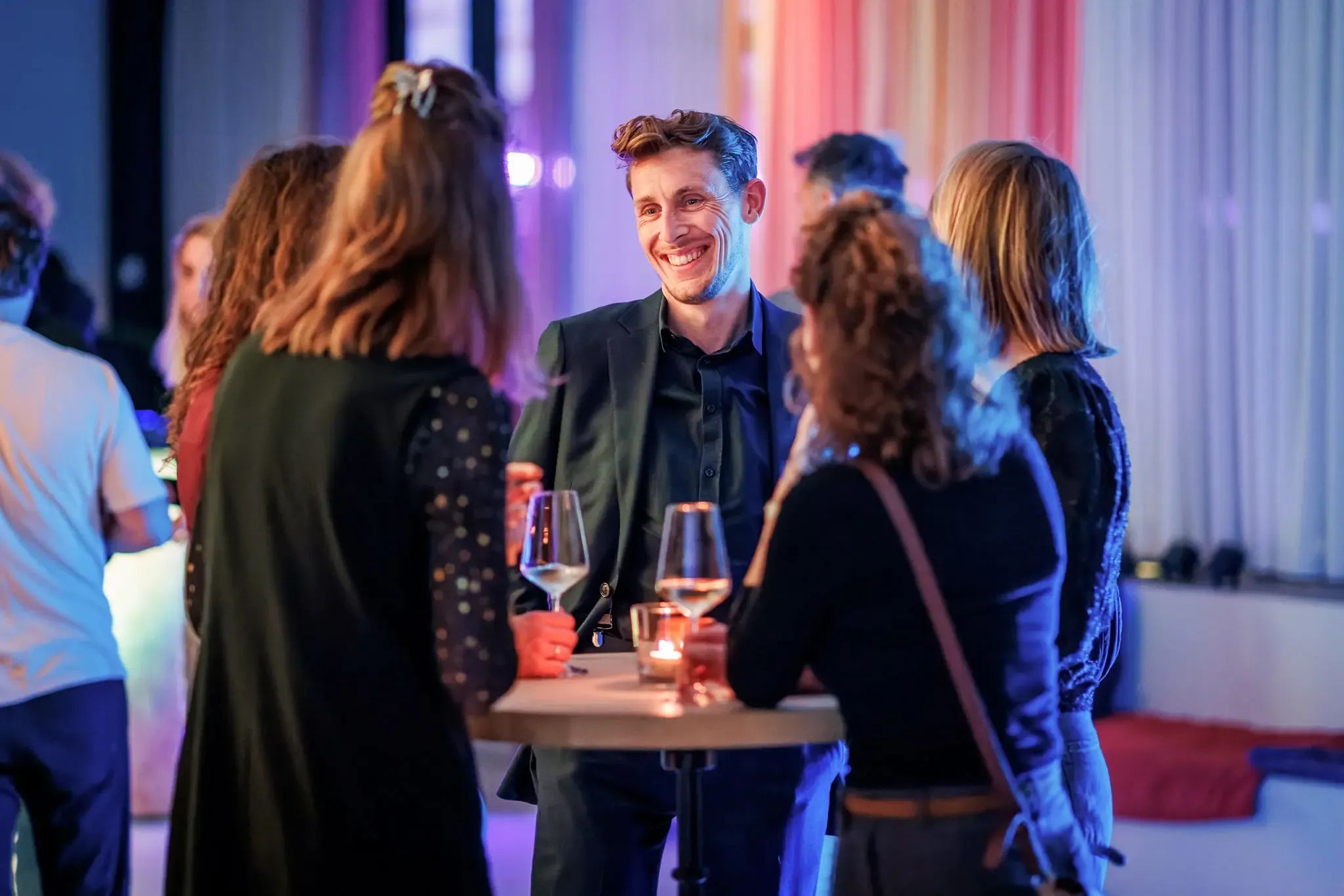 Een glimlachende man praat met vrouwen tijdens een gezellig samenzijn met drankjes