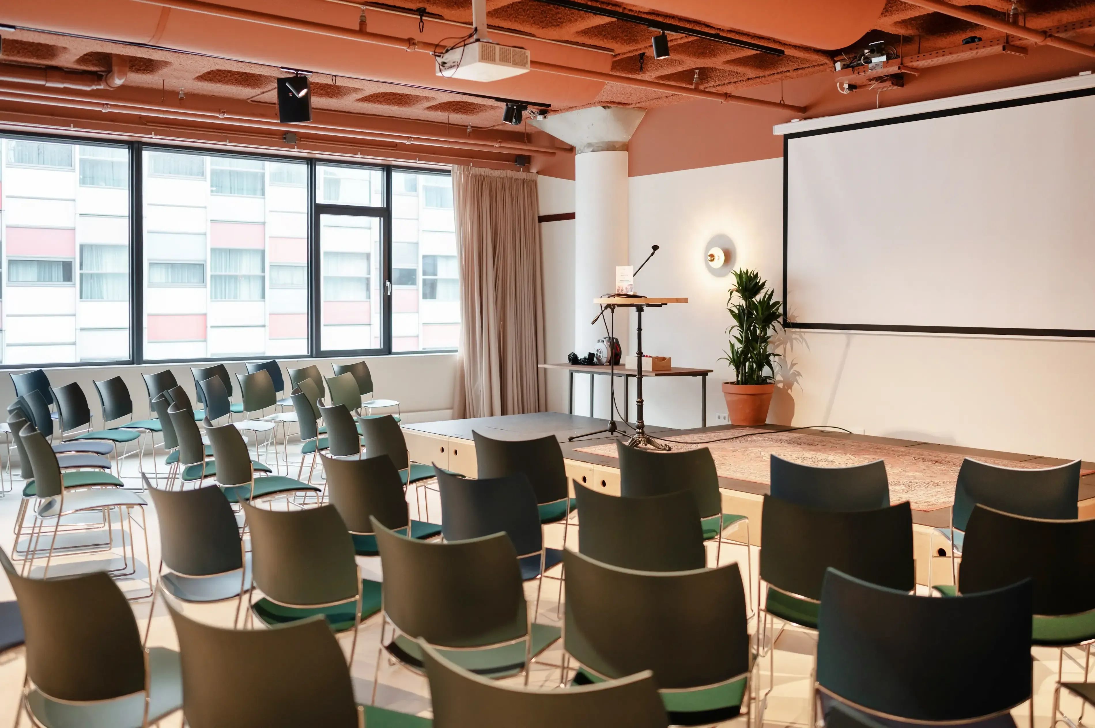 Een lege, moderne vergaderzaal met rijen stoelen die naar een groot projectiescherm zijn gericht.