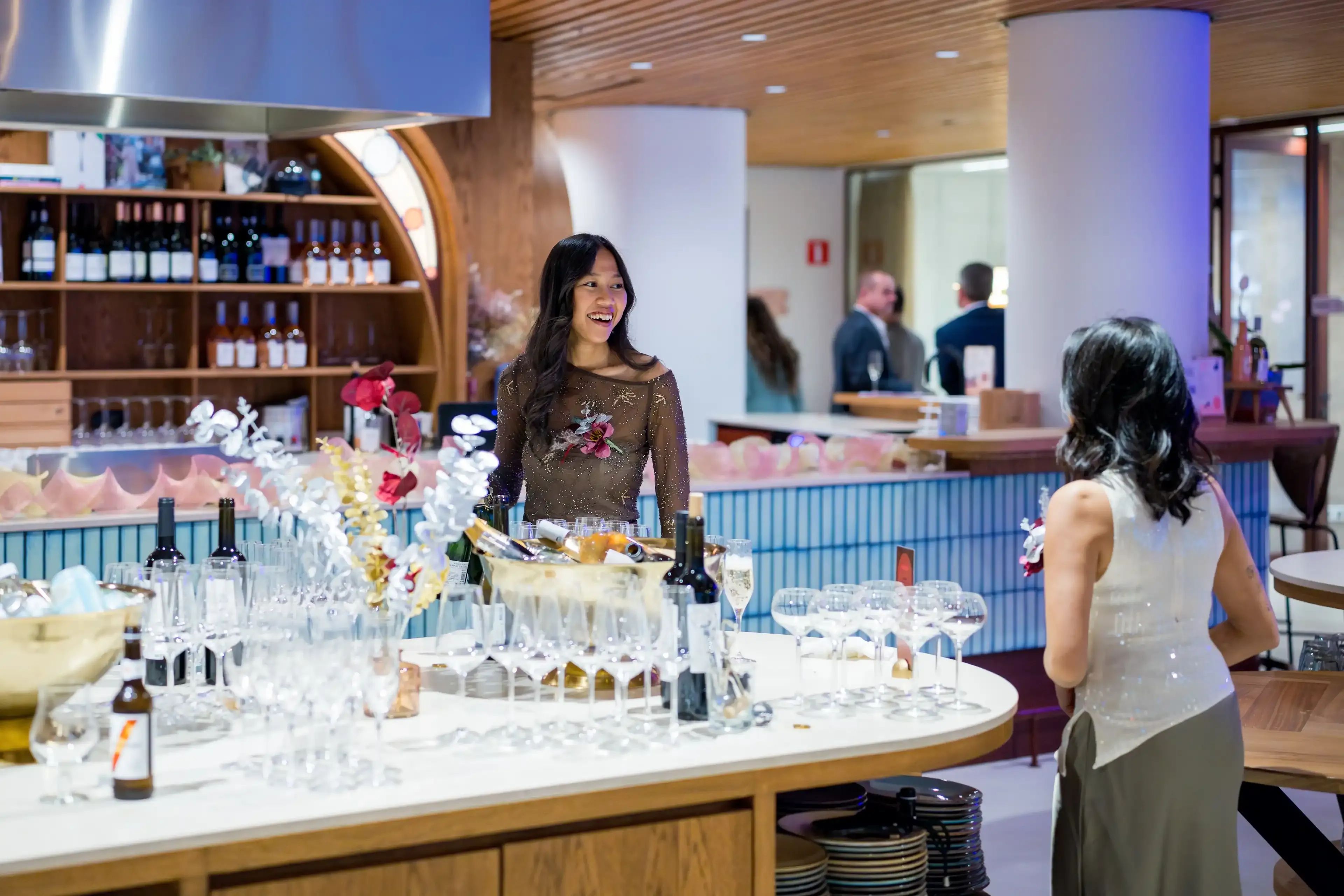 Een glimlachende vrouw serveert drankjes aan een goed gevulde bar tijdens een sociaal evenement.