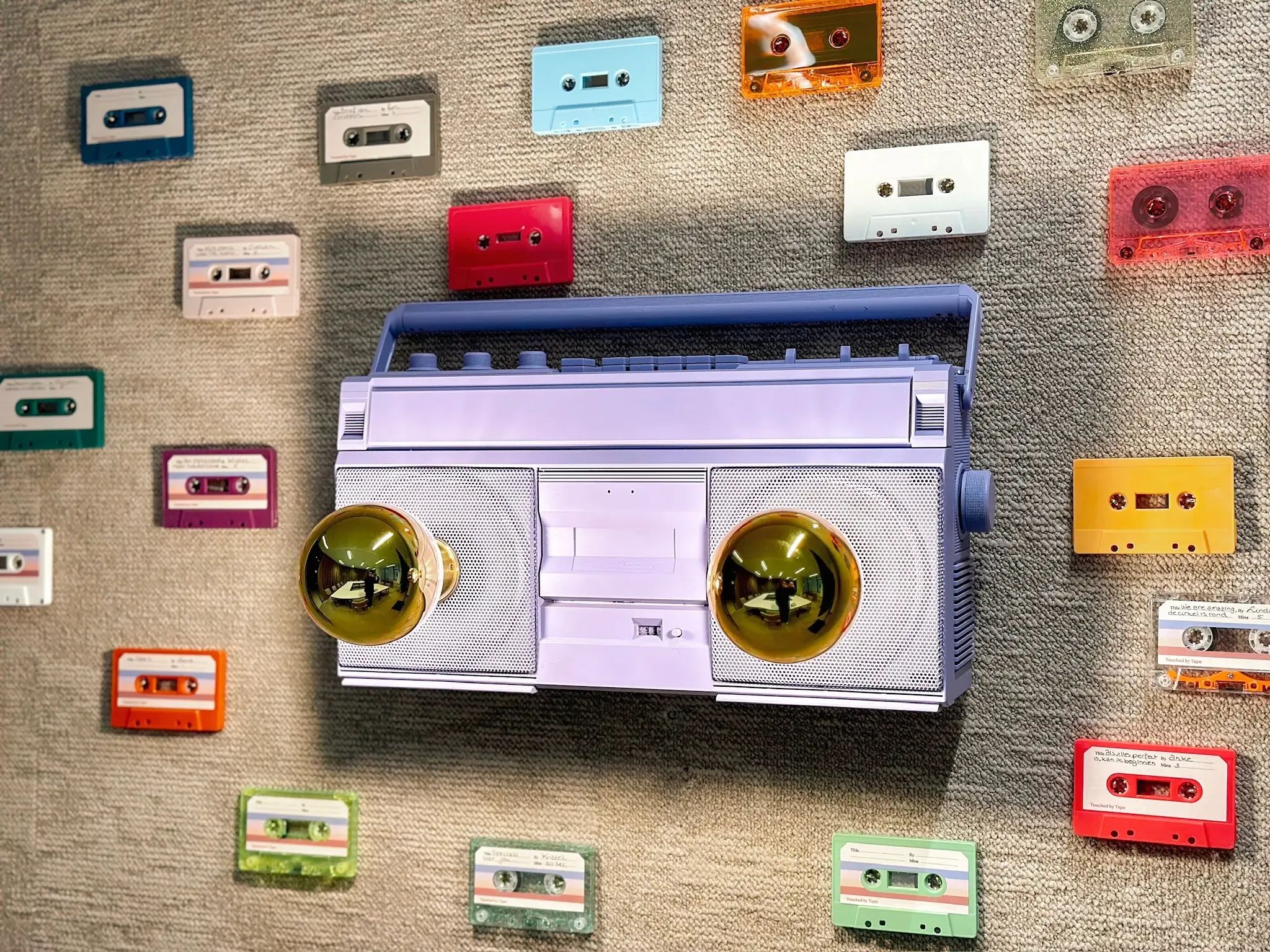 Paarse casettespeler omringd door vele kleurrijke audiocassettes op een gestructureerde muur.