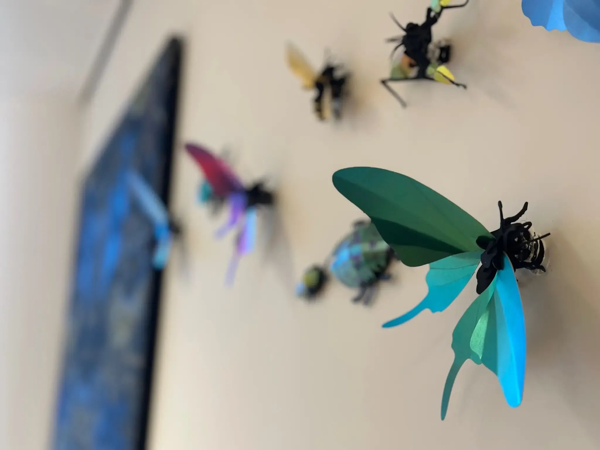 Decoratieve insecten met levendige groene, blauwe en roze vleugels sieren een lichtgekleurde muur.