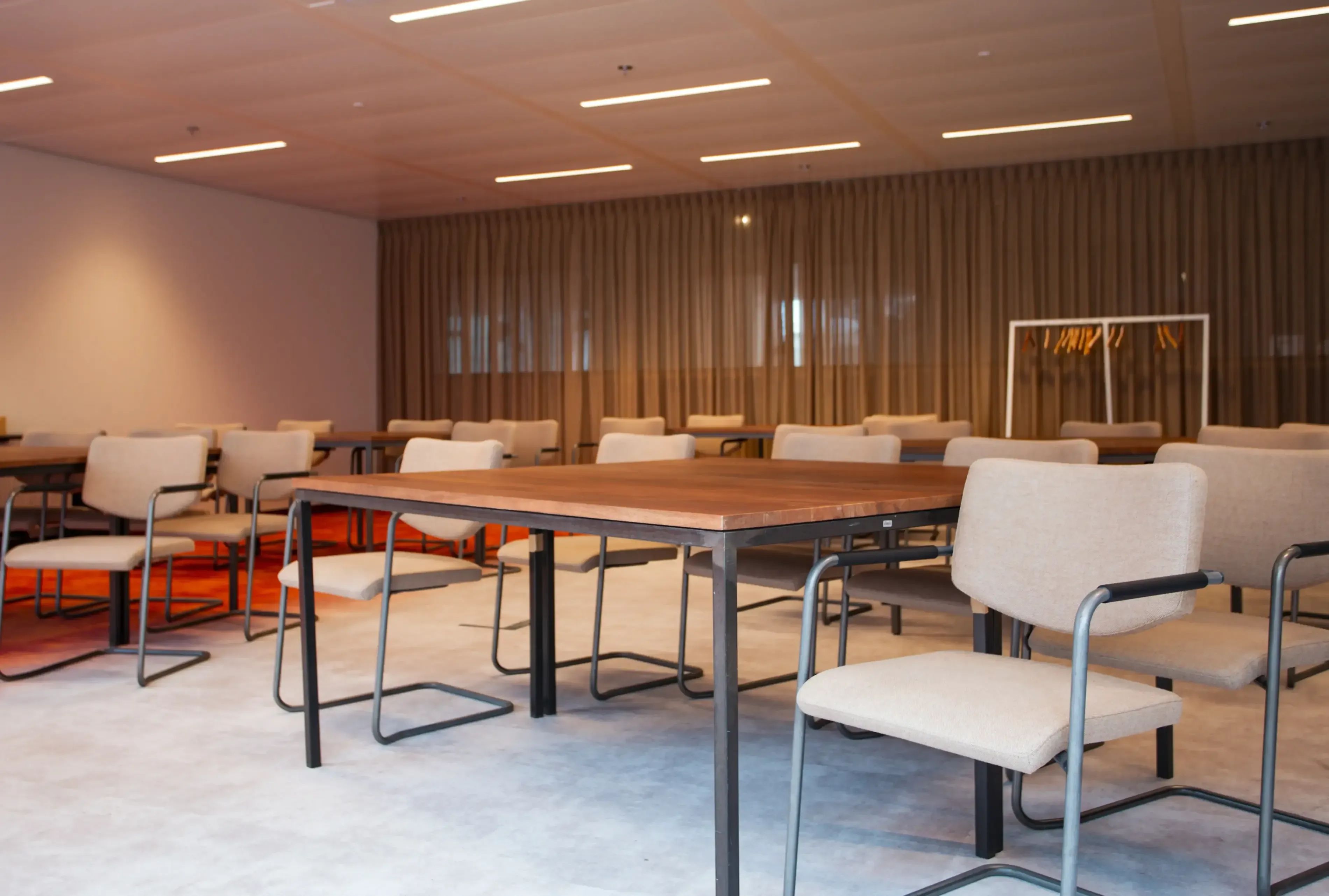 Moderne vergaderruimte met meerdere houten tafels, beige stoelen en warme verlichting.