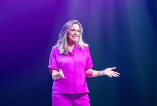 Blonde vrouw in roze outfit op het podium aan het spreken