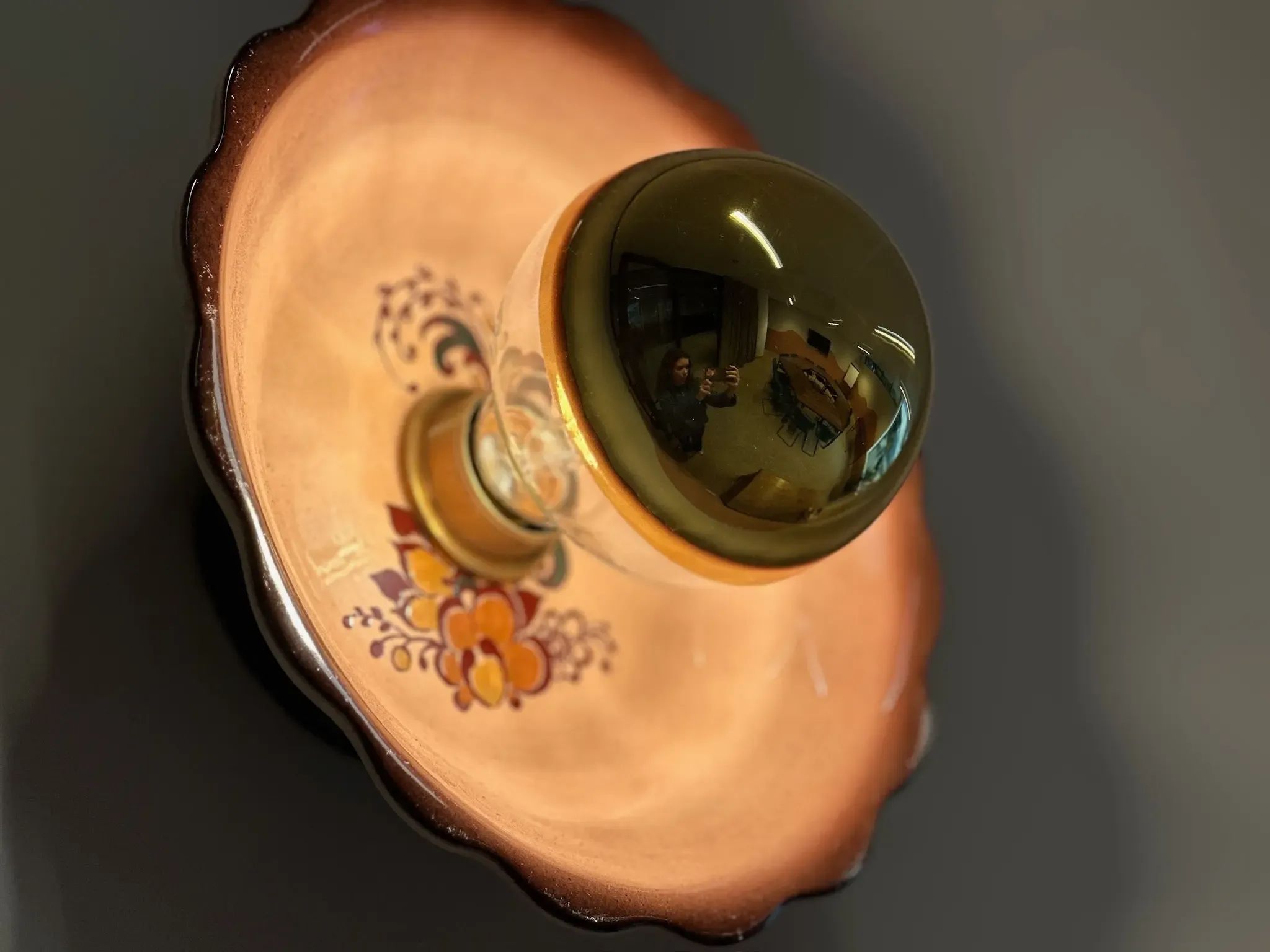 Decoratieve lamp met een keramische kom als voet, bloemmotief en reflecterende groen-gouden gloeilamp.