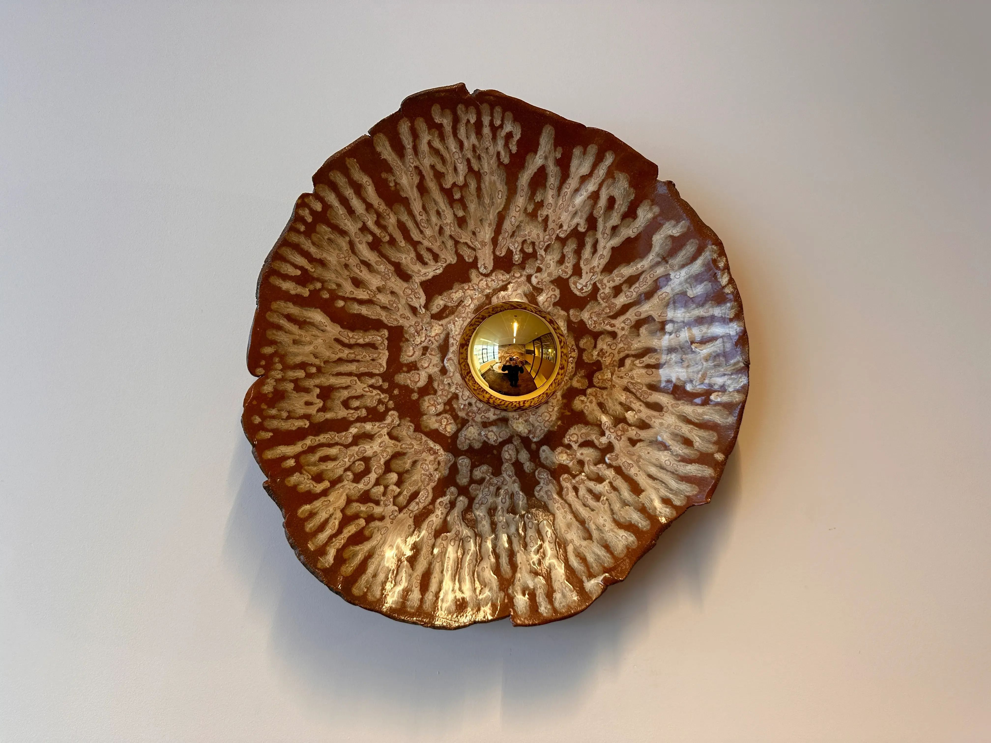 Een paddestoelvormige wandlamp met een gouden lamp en een gestructureerd bruin en wit oppervlak.