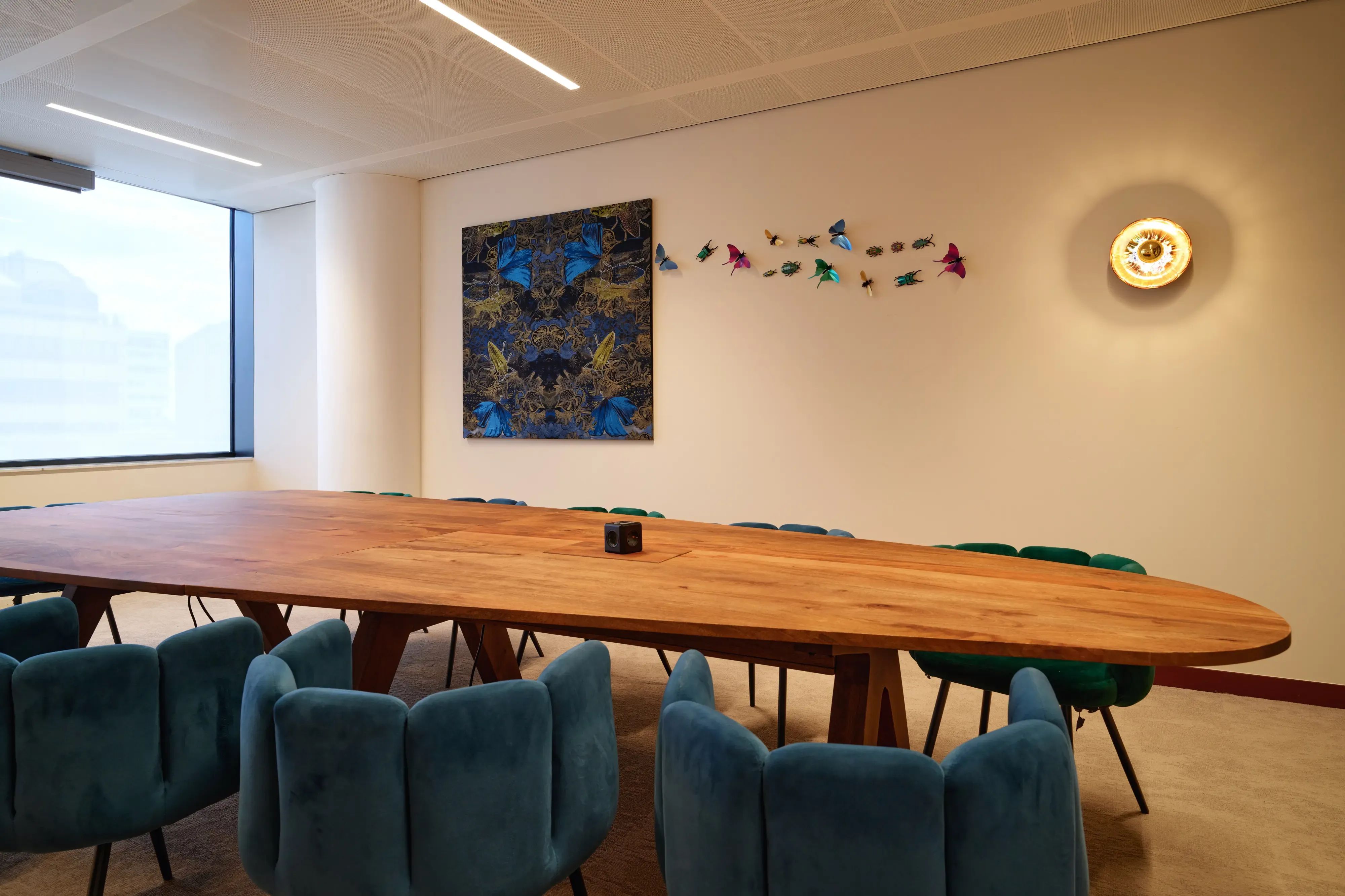 Moderne vergaderruimte met een grote houten tafel, turquoise stoelen en eigentijdse kunst aan de muur.