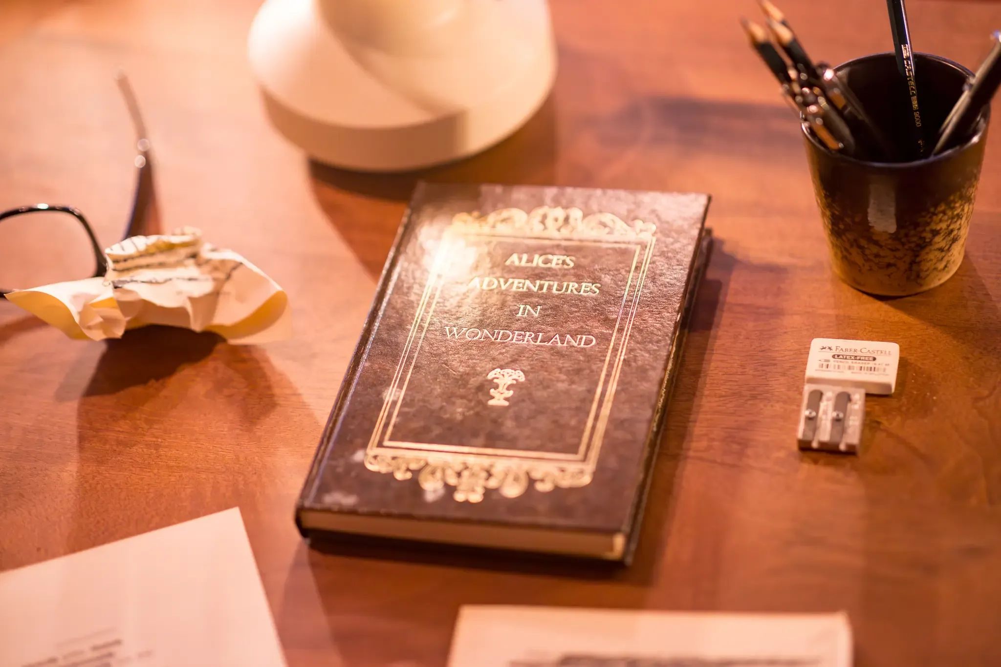 Een oud exemplaar van ‘Alice's Adventures in Wonderland’ op een houten bureau met een bril.